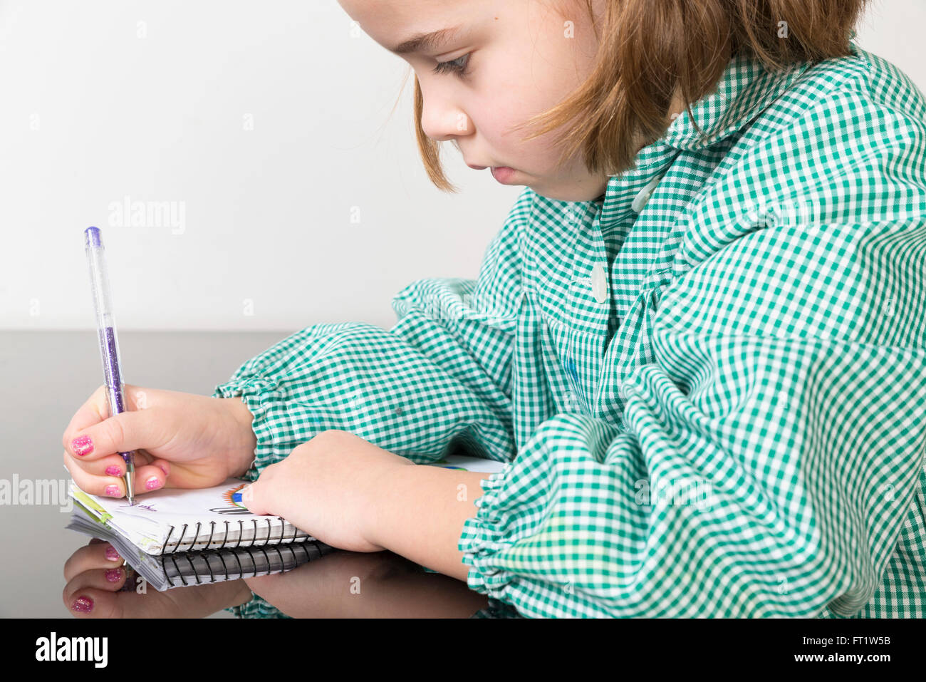Kleines Mädchen mit einem Green plaid Kittel Schreiben und Zeichnen in einem Notebook zu Hause Stockfoto