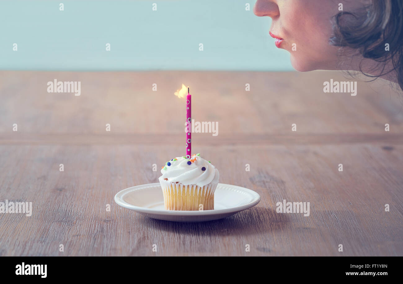 eine Frau Ausblasen einer Kerze auf einen cupcake Stockfoto