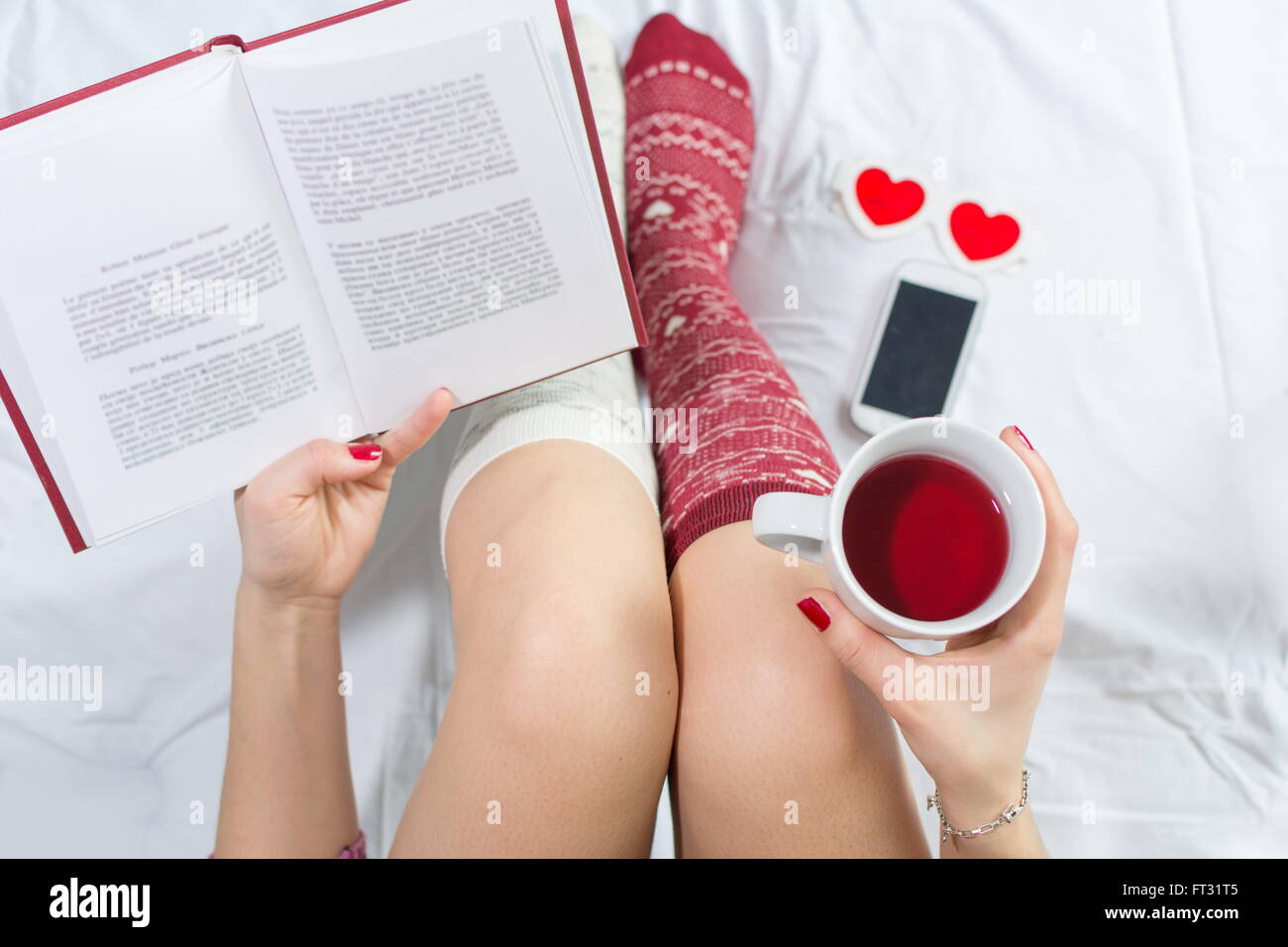 Frau mit einer Tasse Tee im Bett und liest ein Buch Stockfoto