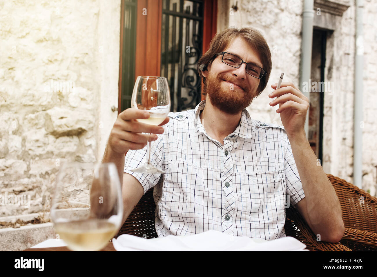 Schöner bärtigen europäischen Mann Wein trinken und Rauchen Zigarette sitzen in Street Cafe. Stockfoto