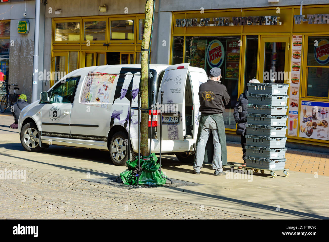 Kristianstad, Schweden - 20. März 2016: Ein männlicher Konditor stehen hinter einer Lieferung Auto und sprechen Sie mit einer Person hinter ein paar Kisten. Stockfoto