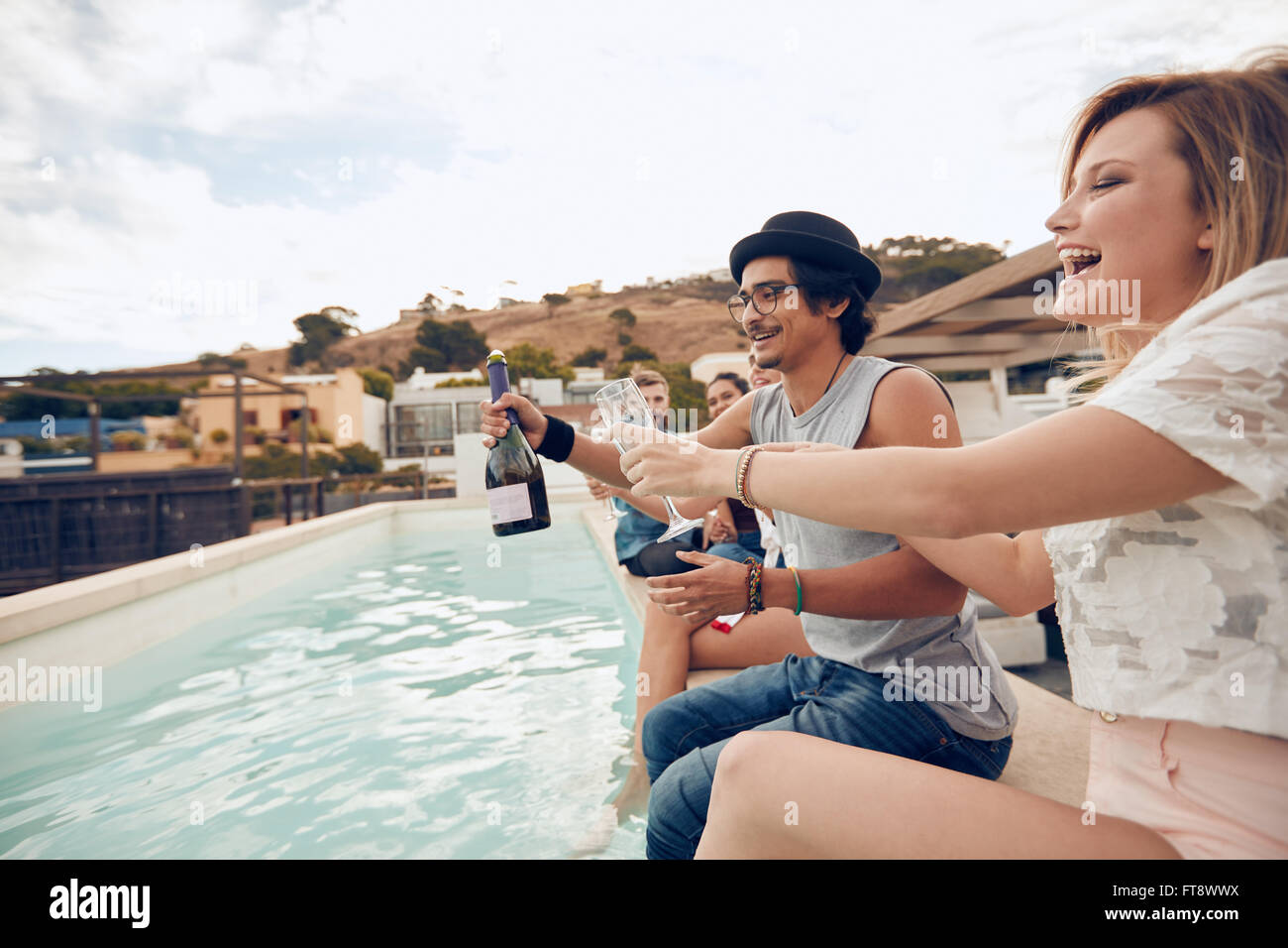 Im Freien Schuss glücklich junger Menschen sitzen auf dem Rand des Pools Champagner trinken. Gemischtrassig Freunden genießen und Toasten Stockfoto