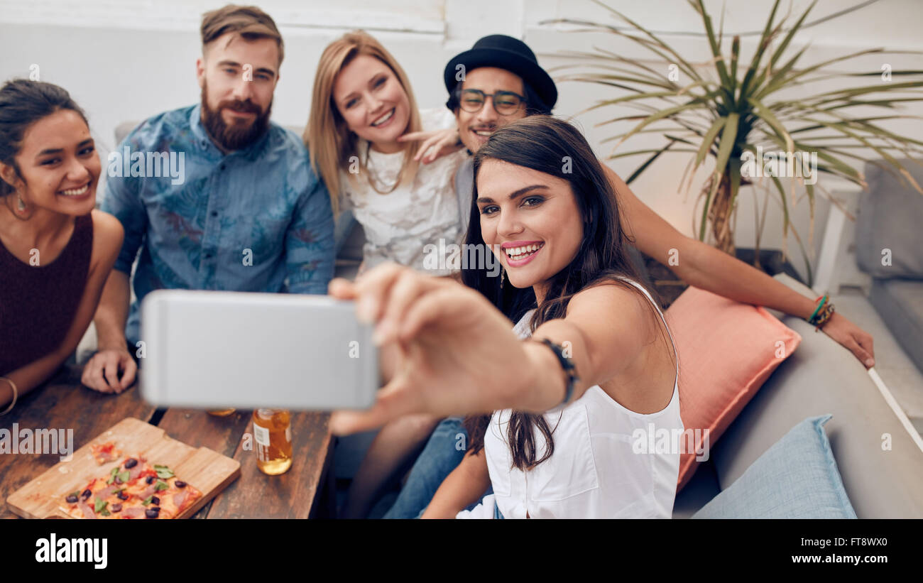 Gemischtrassige Menschen genießen in der Vertragspartei, die ein Selbstporträt mit Handy. Gruppe junger Freunde auf Couch nehmen se Stockfoto