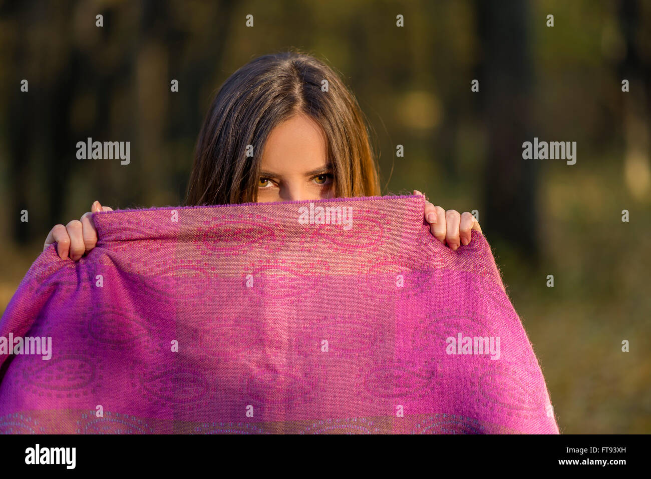 Hinter lila Schal. Hübsche Teenager Mädchen mit braunen Augen bedeckt ihr Gesicht mit dem lila Schal im Nachmittag Wald. Stockfoto
