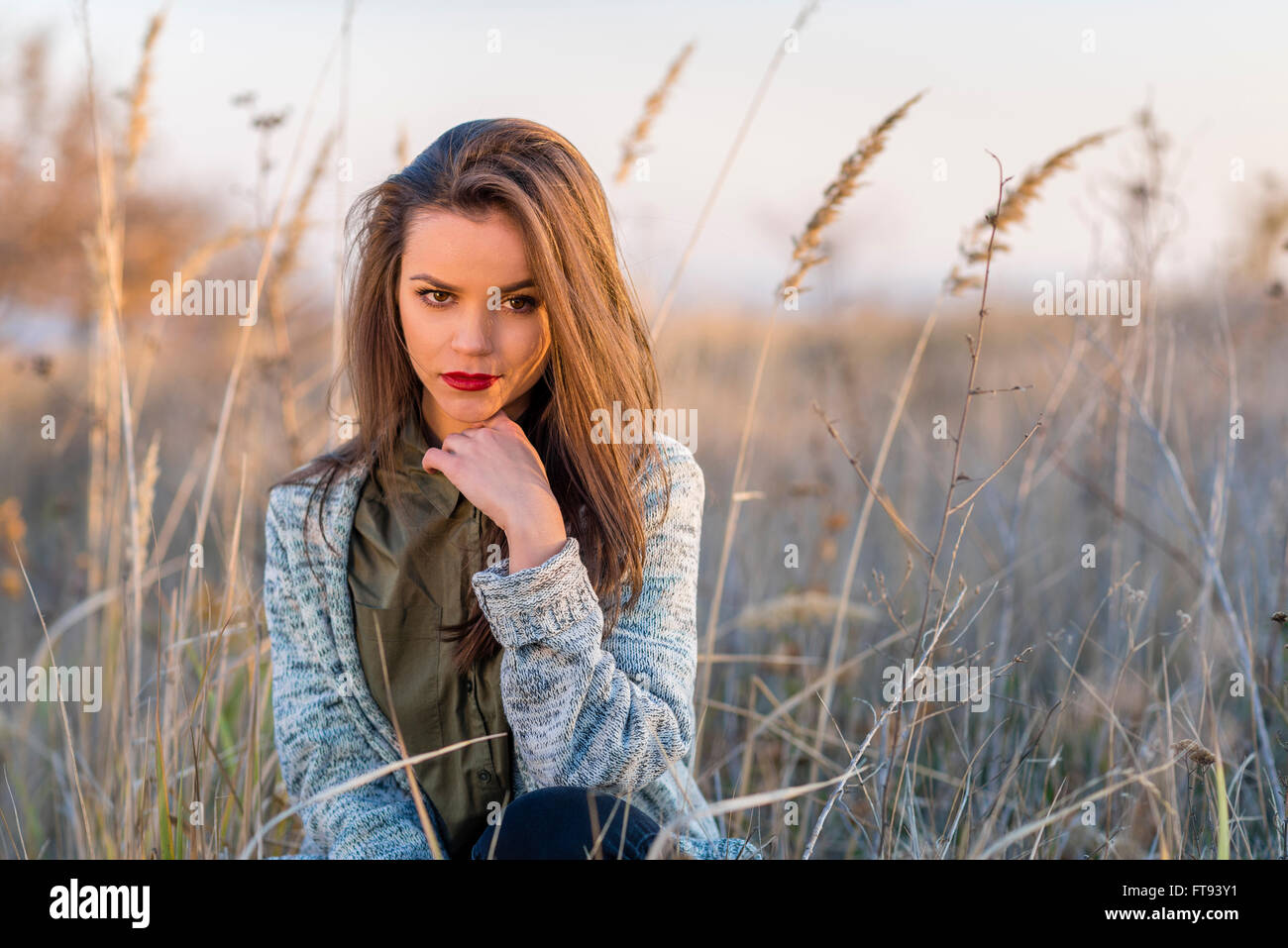 Selbstbewusst aussehen. Ein schöne Teenager selbst zuversichtlich Mädchen sitzt in einem Feld. Mädchen hat braune Augen und Haare und rote Lippen. Stockfoto