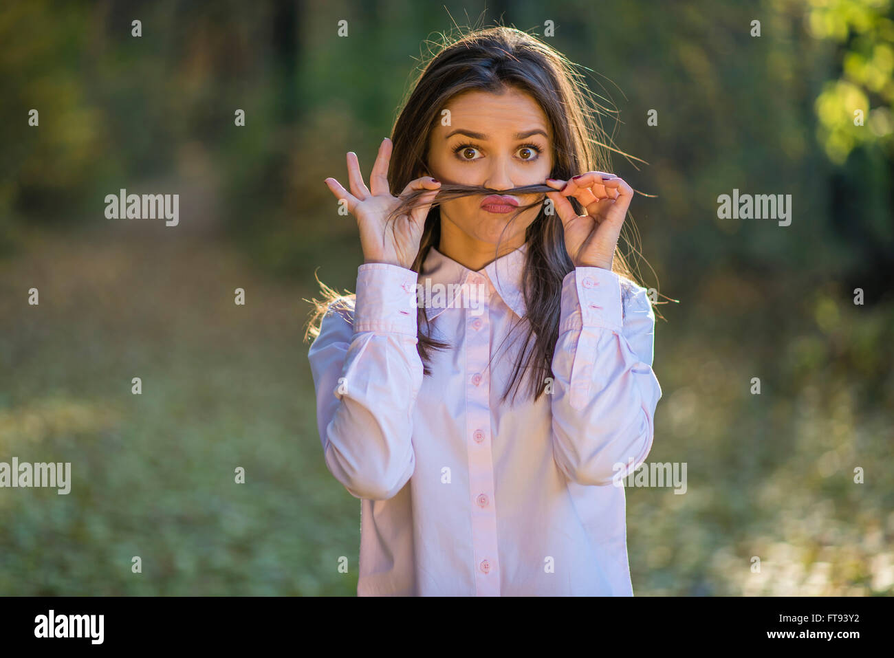 Ein junges Mädchen macht Schnurrbart aus ihrem Haar mit weit aufgerissenen Augen und einen skurrilen Ausdruck auf ihrem Gesicht. Stockfoto