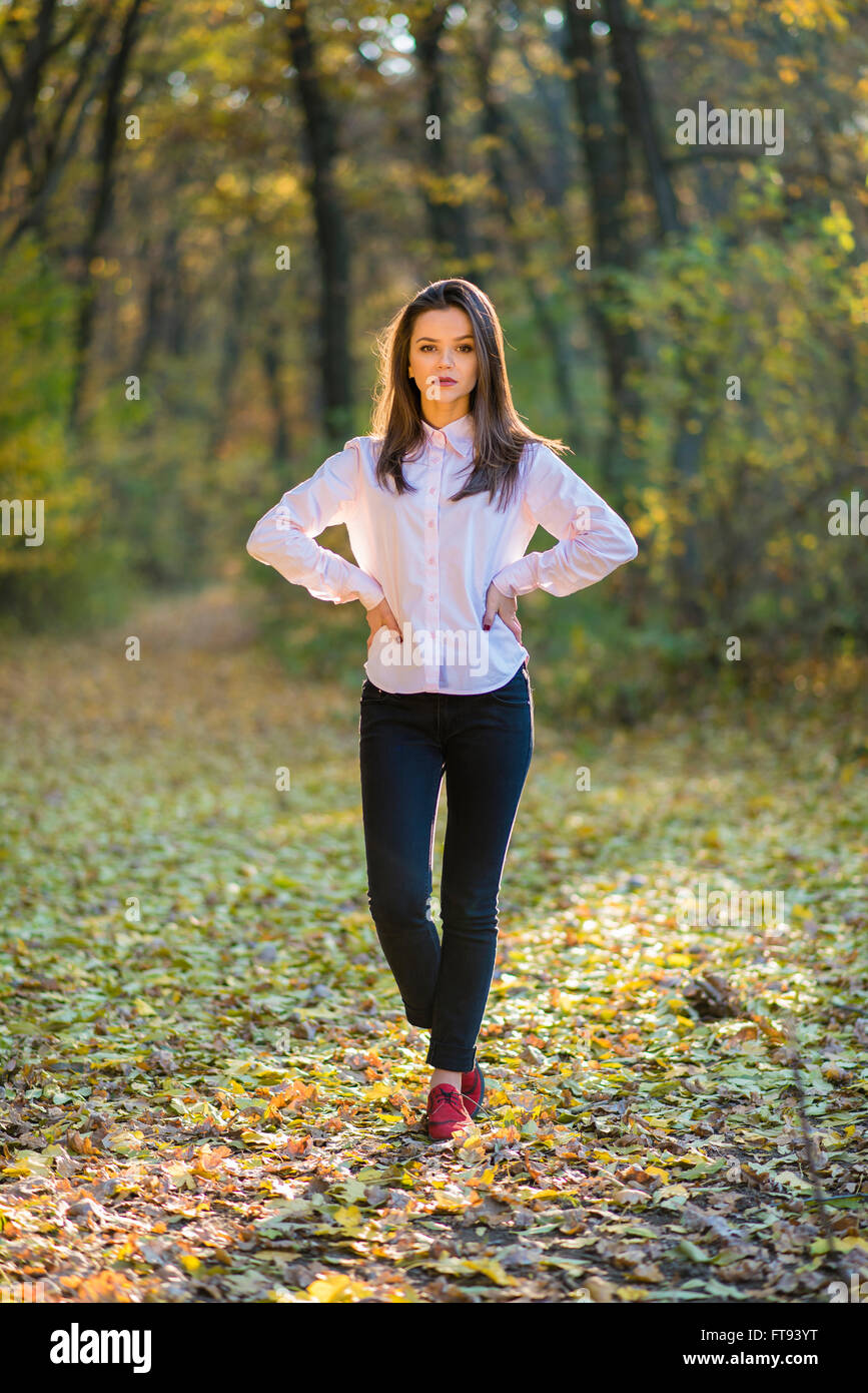 Posing auf Wanderweg im Wald. Eine ernste aussehende Mädchen posiert in  einem rosa Hemd, dunkelblaue Jeans und rote Schuhe im Vordergrund ein  Herbst Stockfotografie - Alamy