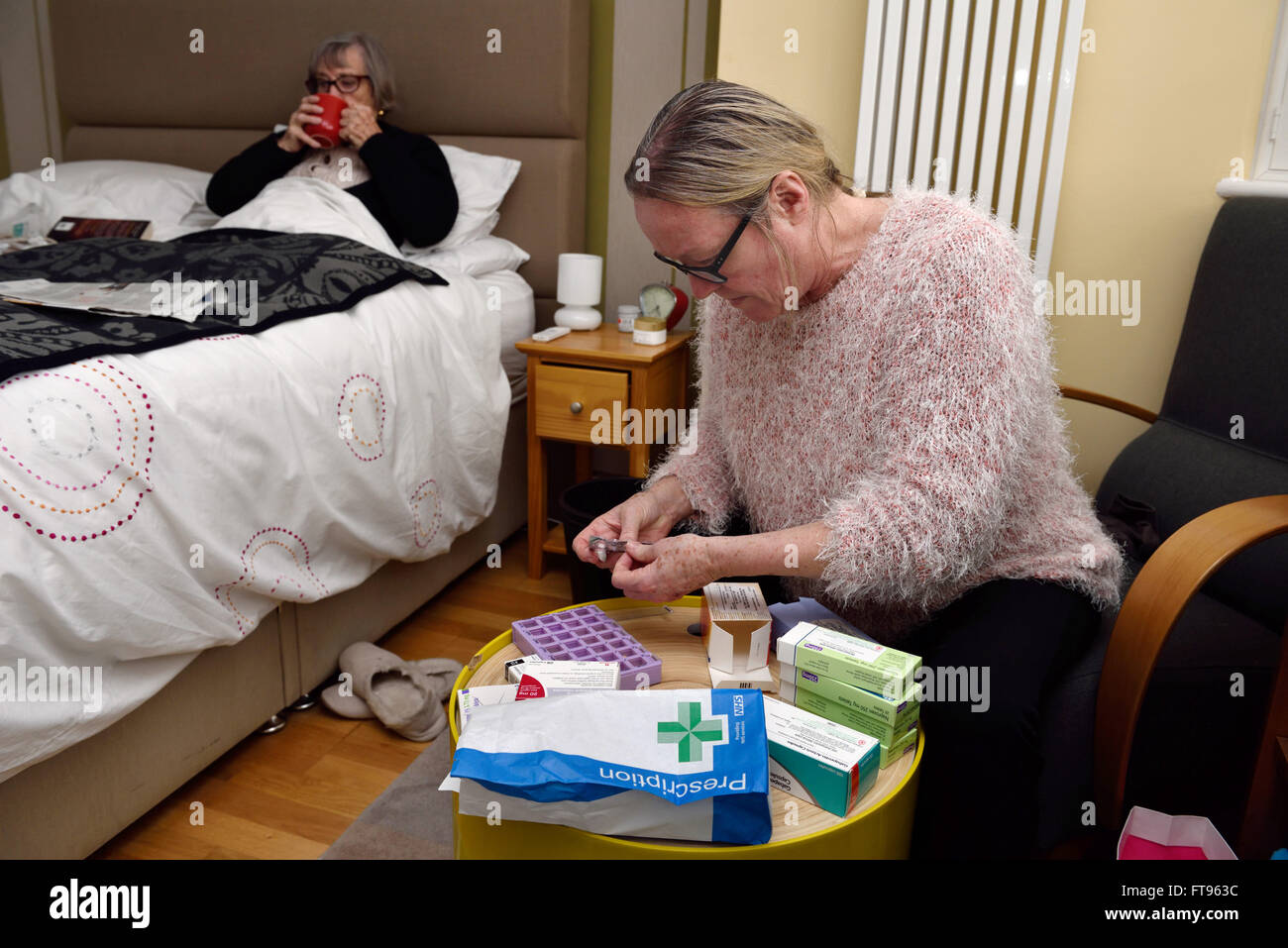 Eine ältere Frau sitzt in ihrem Bett sein betreut in ihrem Haus ihrer Tochter, die ihr prüft viele Boxen von Medikamenten. Stockfoto