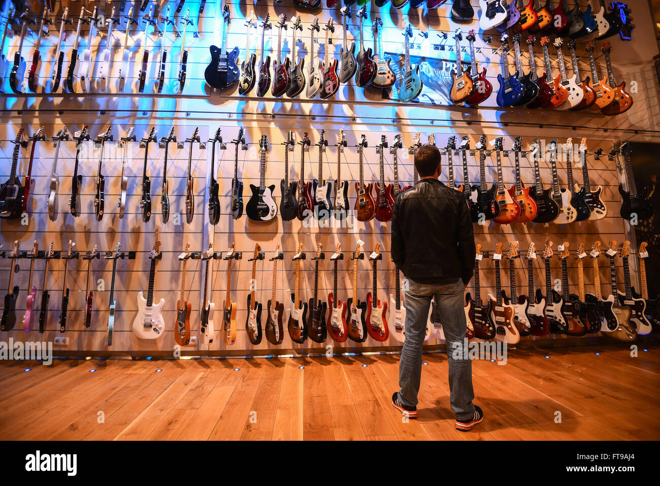 Treppendorf, Deutschland. 24. März 2016. Ein Kunde steht vor einer Wand von  Gitarren im Musikhaus Thomann in Treppendorf, Deutschland, 24. März 2016.  Das Musikhaus Thomann ist eines der weltweit größten Online-Händler in