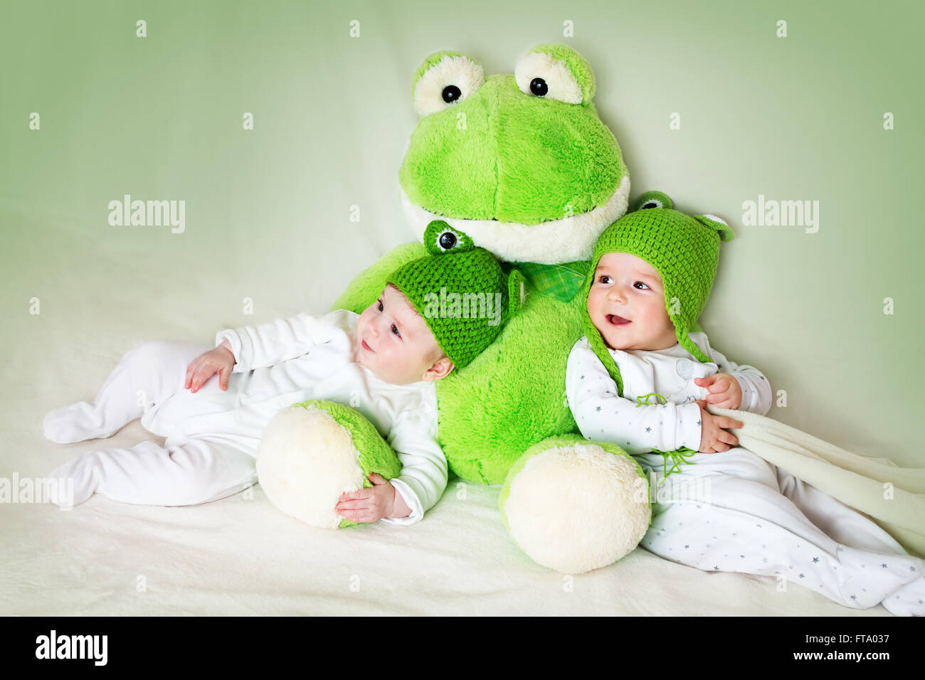 zwei niedliche Babys im Frosch-Hüte mit einem Stofftier liegend Stockfoto