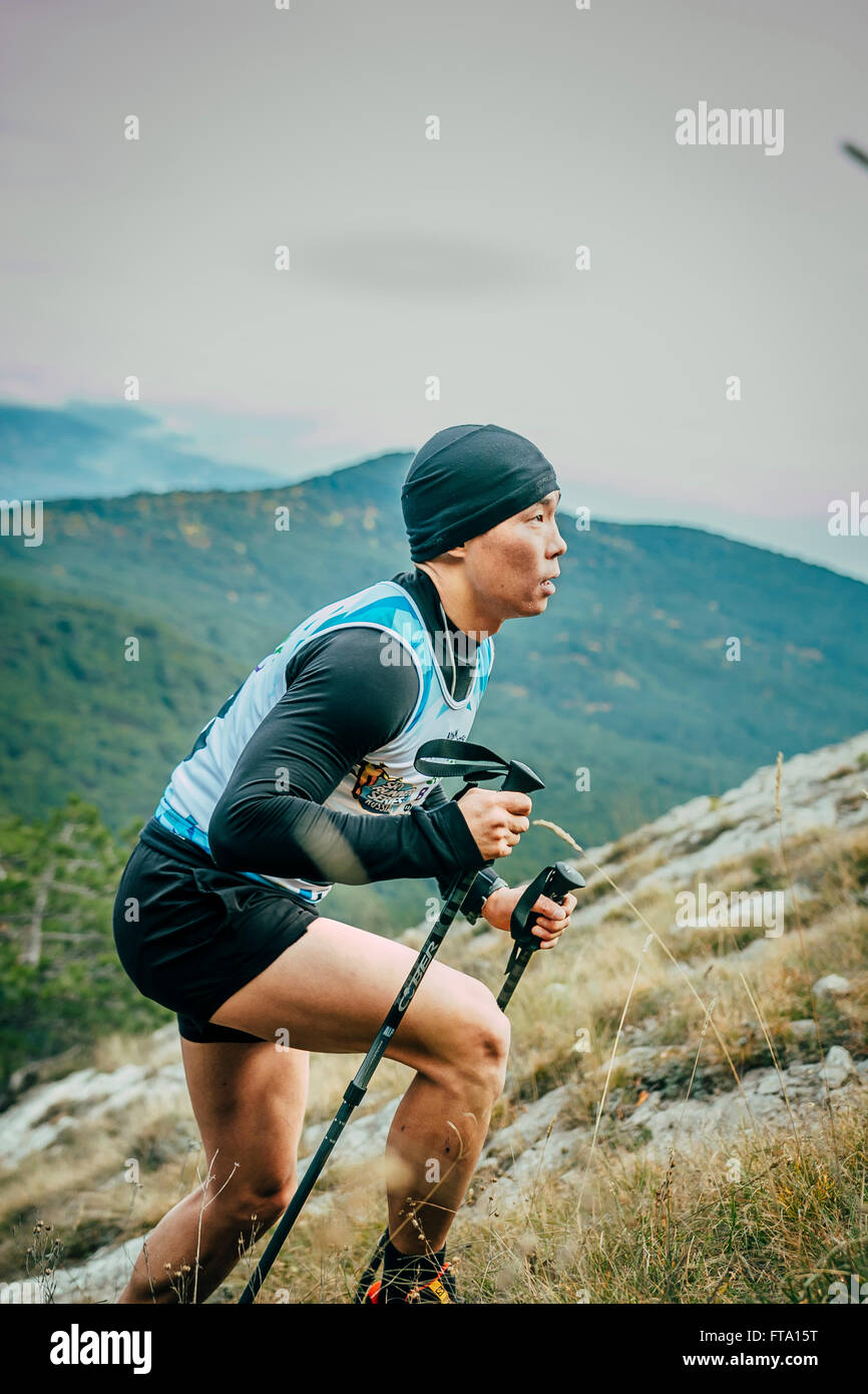 junge Sportler mit nordic-walking-Stöcke ist auf Seite des Mountainduring Mountain marathon Stockfoto