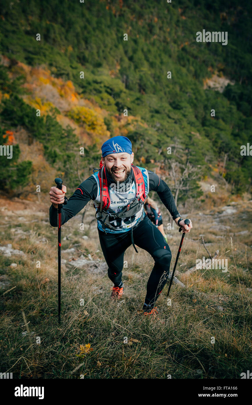 freudiger junger Athlet besteigt einen Berg mit nordic-walking-Stöcke während Bergmarathon Stockfoto