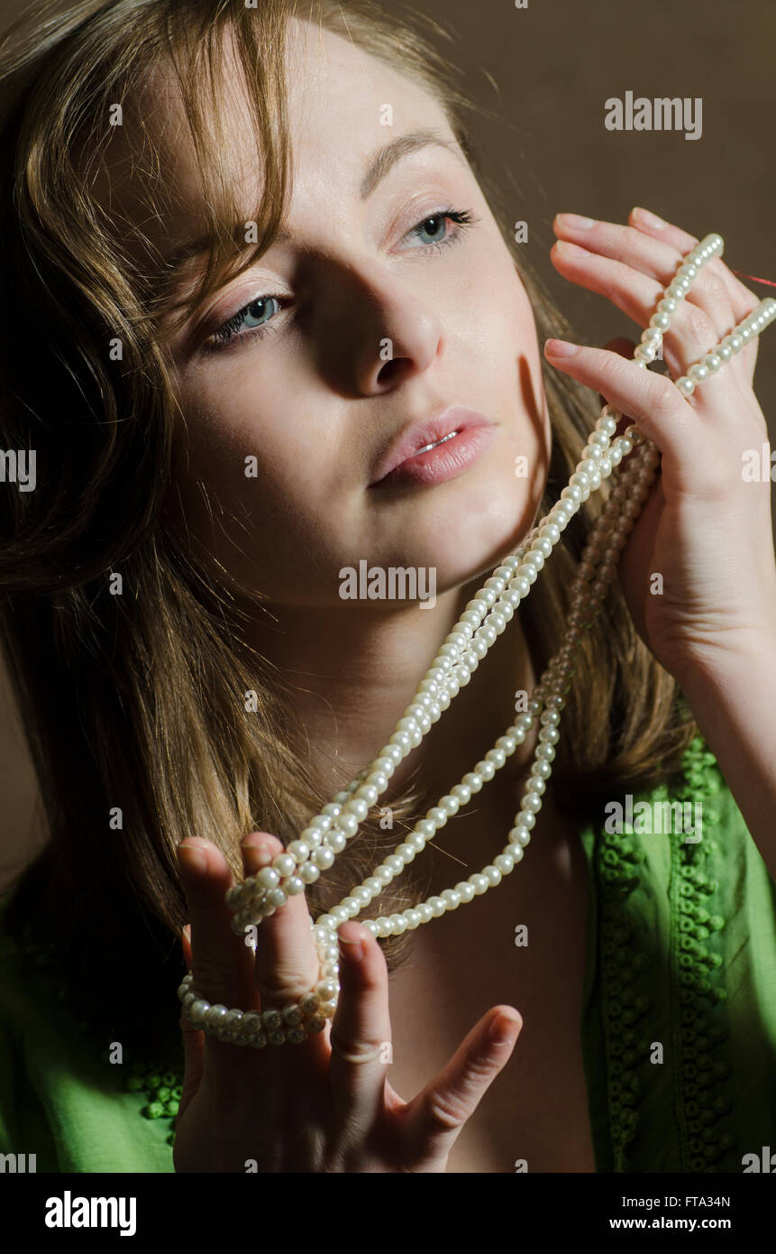 Schöne junge Frau hält eine Perlenkette wegschauen Stockfoto