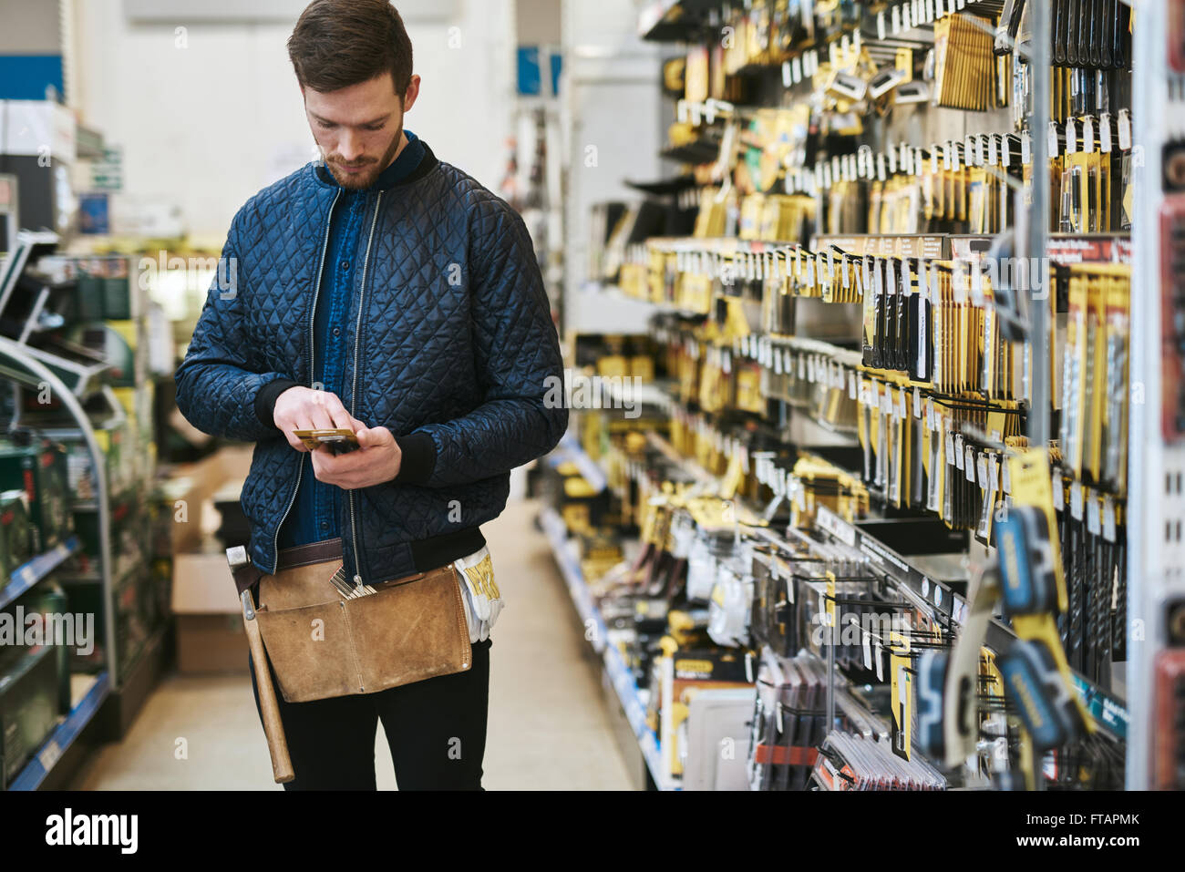 Junge Handwerker prüfen Informationen auf seinem Handy vor dem Kauf in einem Baumarkt Stockfoto