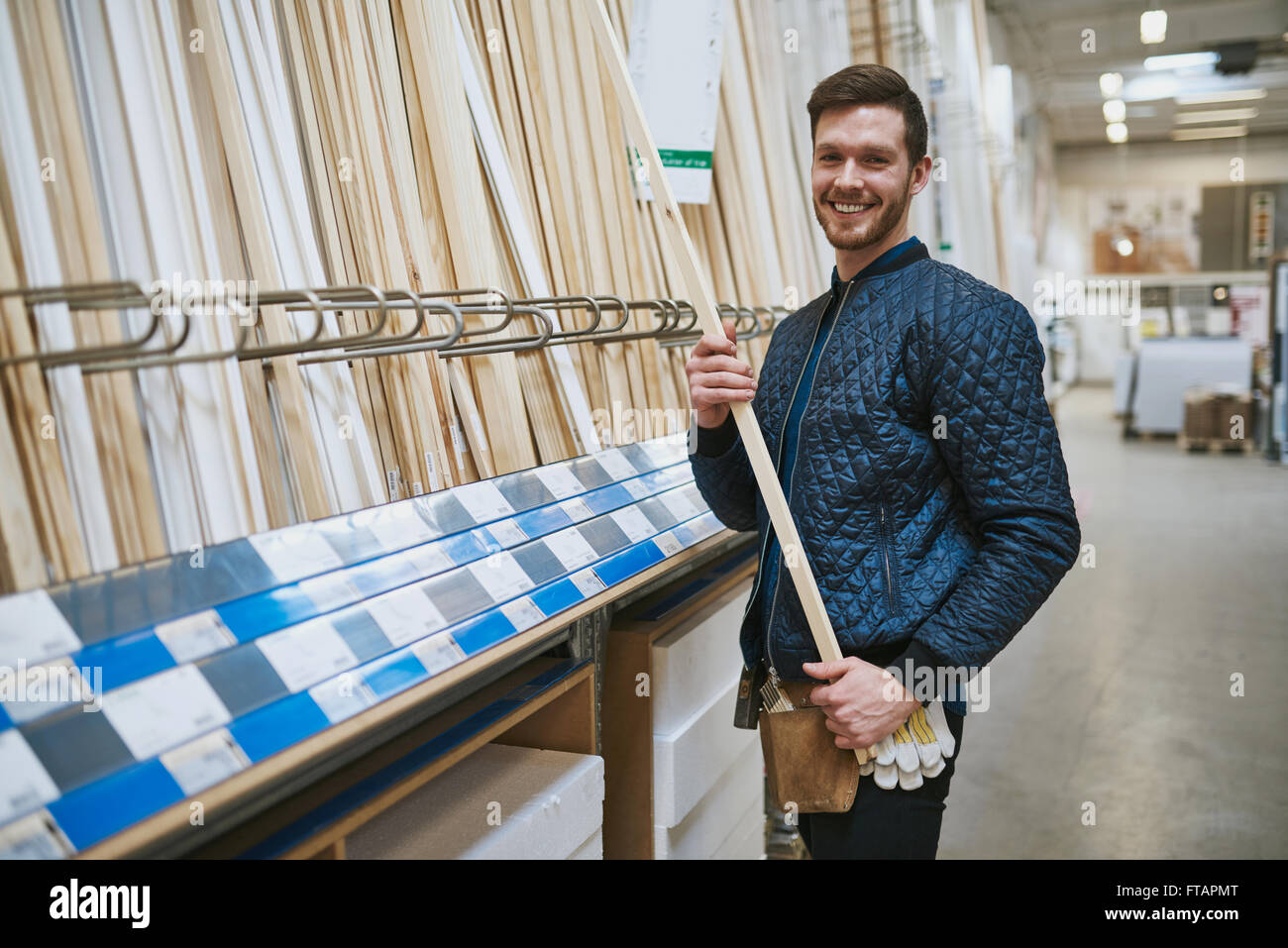 Happy selbstbewussten jungen Tischler oder Handwerker stehen in einem Hardware Store Einkauf Längen von Schnittholz aus den Regalen Stockfoto