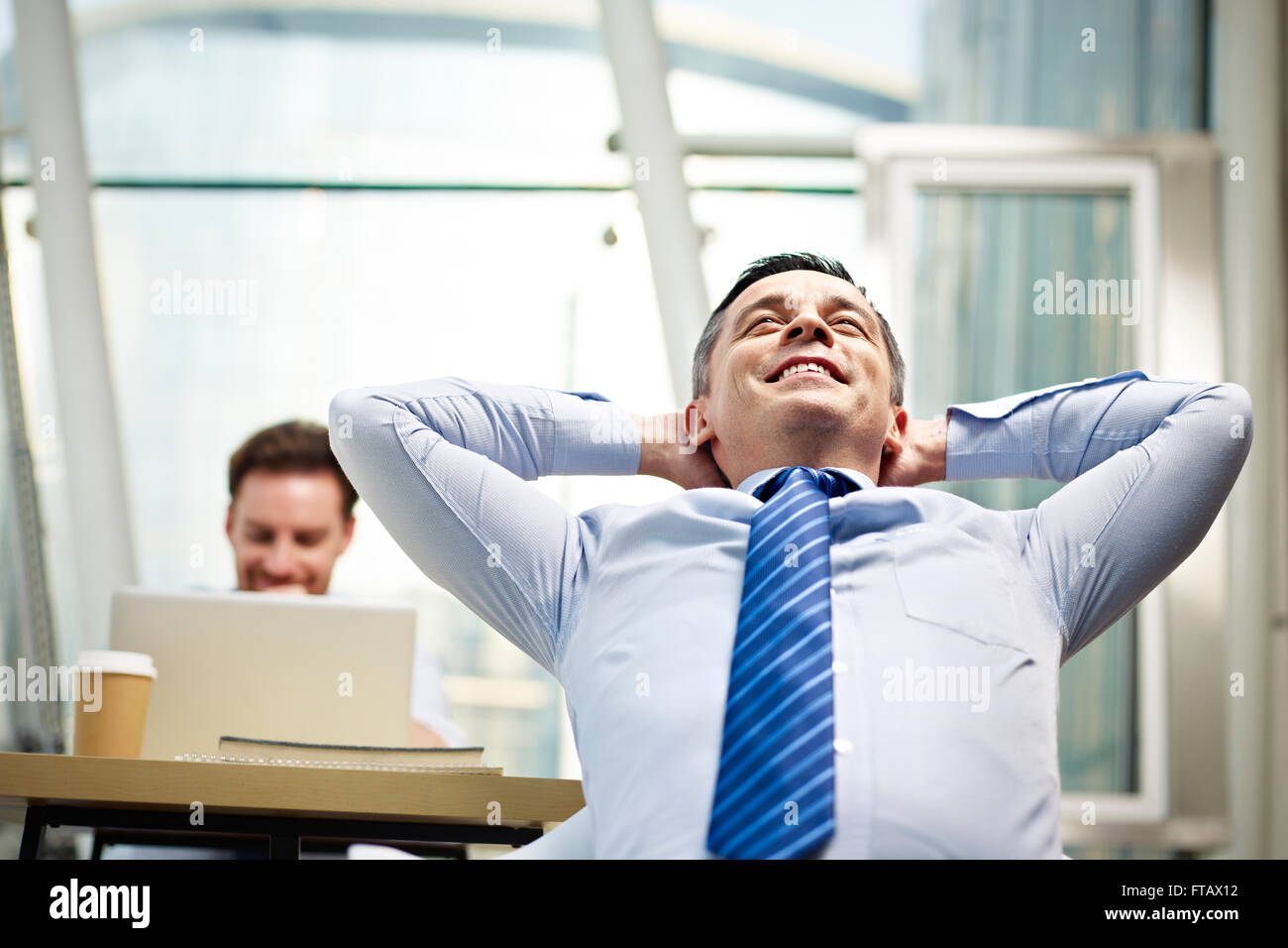 Unternehmer im Büro denken Tagträumen Hände hinter Kopf sitzen. Stockfoto