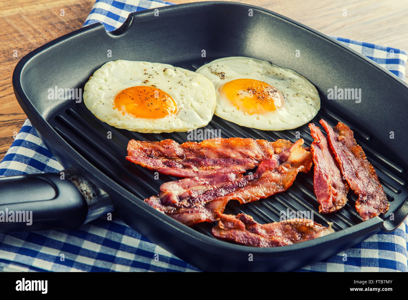 Schinken und Ei. Speck und Ei. Ei gesalzen und mit schwarzem Pfeffer bestreut. Englisches Frühstück. Gegrillter Speck, Ei in Pfanne Stockfoto