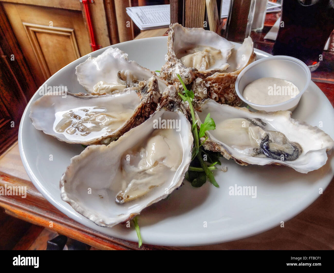 einige geöffneten Austern auf einem weißen Teller mit Bad im hölzernen Ambiente Stockfoto