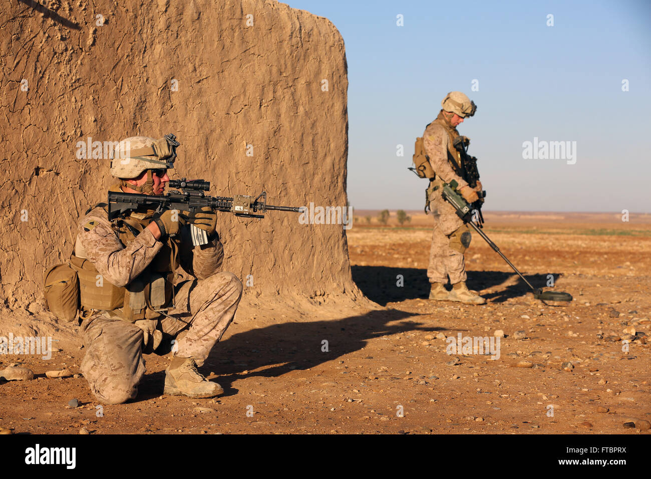 Ein US-Marine gilt Sicherheit als Fellow Marine für improvisierte explosive Vorrichtungen mit einem Metalldetektor während einer Patrouille Mission 15. Januar 2014 in der Nähe von Spin Boldak, Afghanistan fegt. Stockfoto