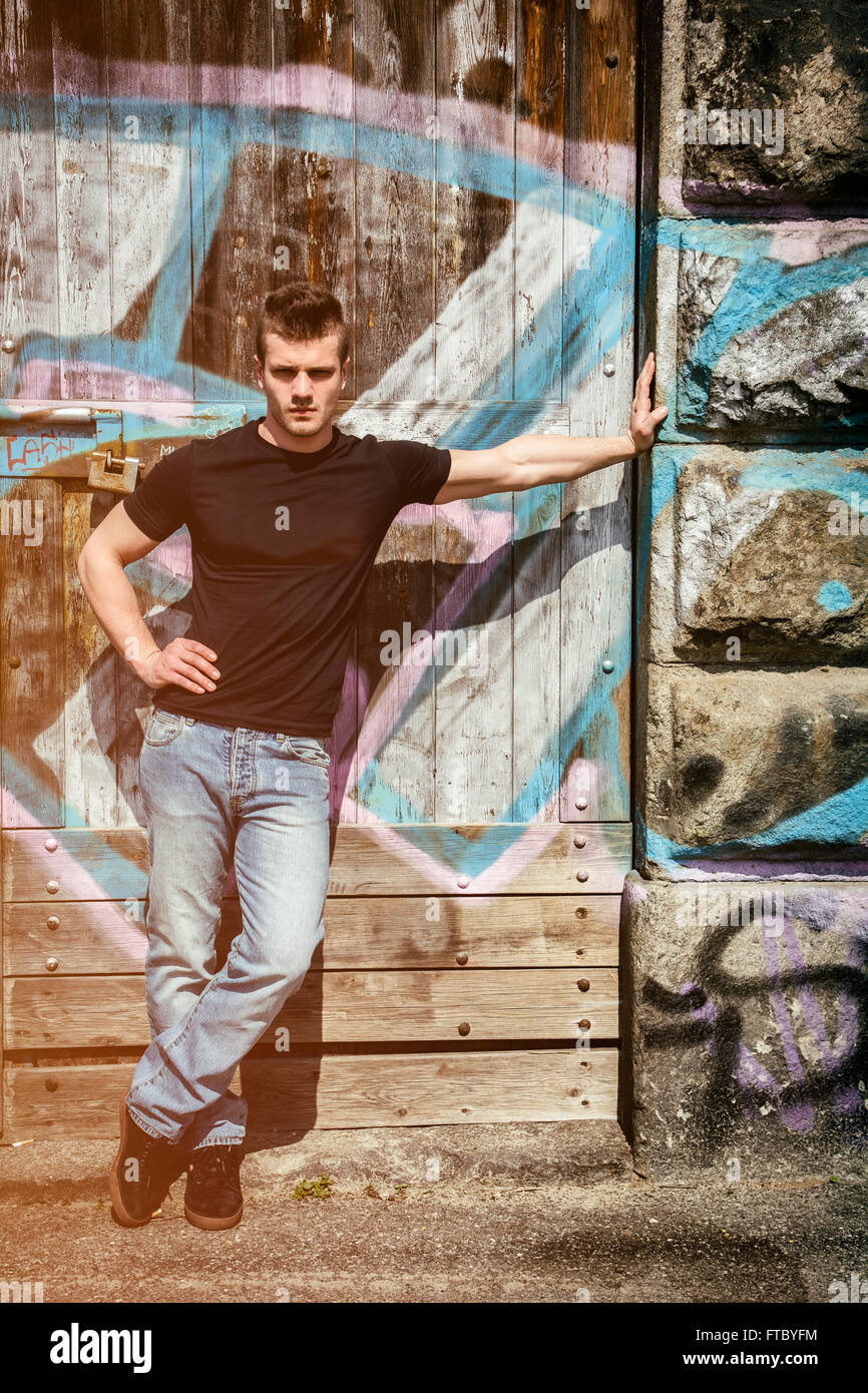 Attraktive junge Mann stehend an bunten Graffiti-Wand, Blick in die Kamera. Gedreht in voller Länge Stockfoto