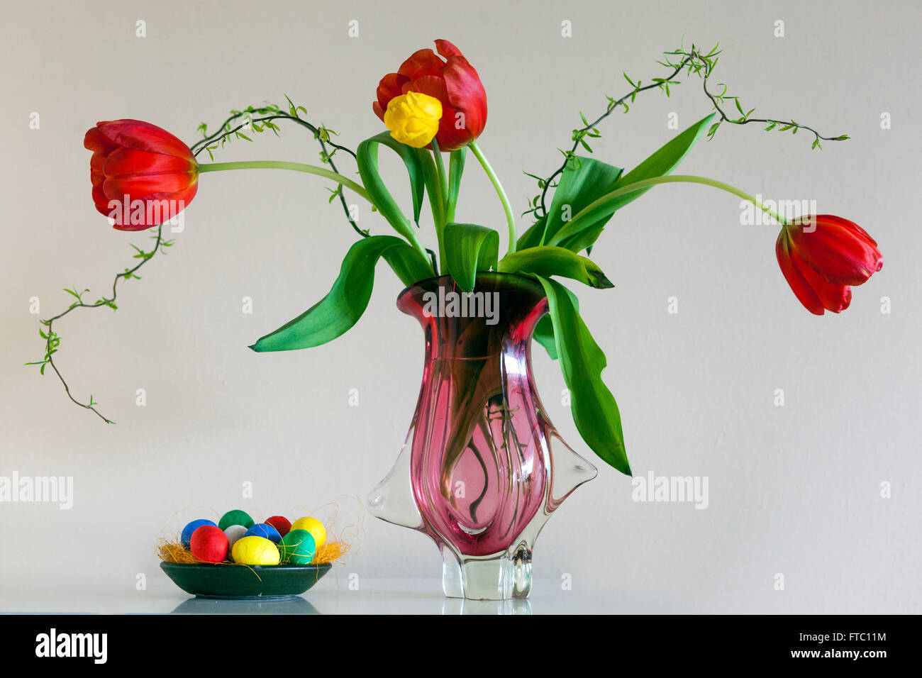 Blühende Tulpen in Vase mit weißem Hintergrund und farbigen Ostereiern Stockfoto