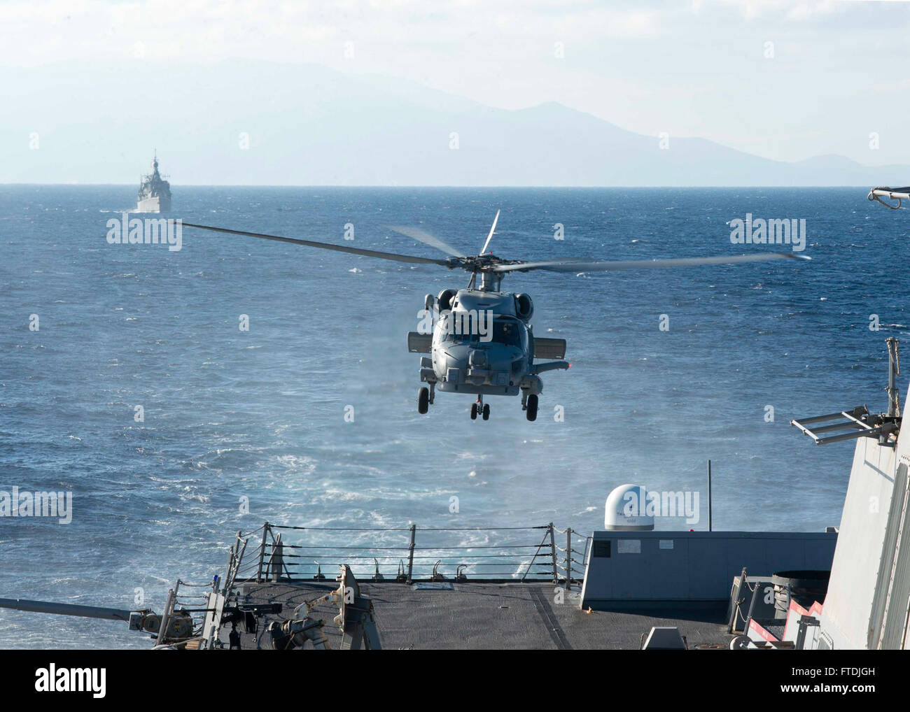 Dieses Bild vom 6. Dezember 2015 zeigt einen MH-60R Sea Hawk Helikopter, der von der USS Bulkeley (DDG 84), einem Raketenzerstörer, abhebt, mit der HS Aigaion (F 460), einer Fregatte der Elli-Klasse der Hellenischen Marine, im Hintergrund während einer Marineübung in der Ägäis. Stockfoto