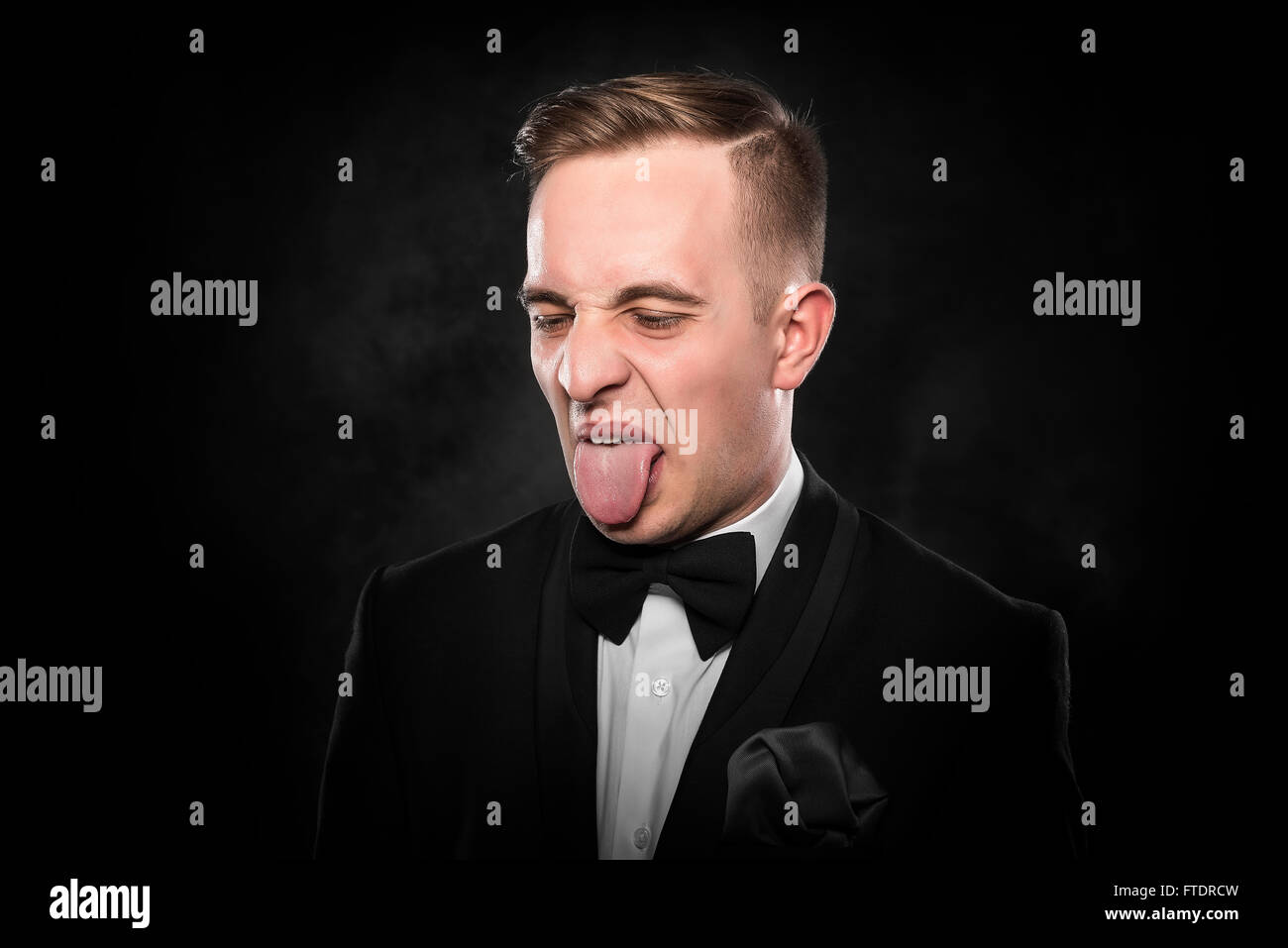 Geschäftsmann im Anzug zeigt Zunge. Negativen menschlichen Emotionen auf dunklem Hintergrund. Stockfoto