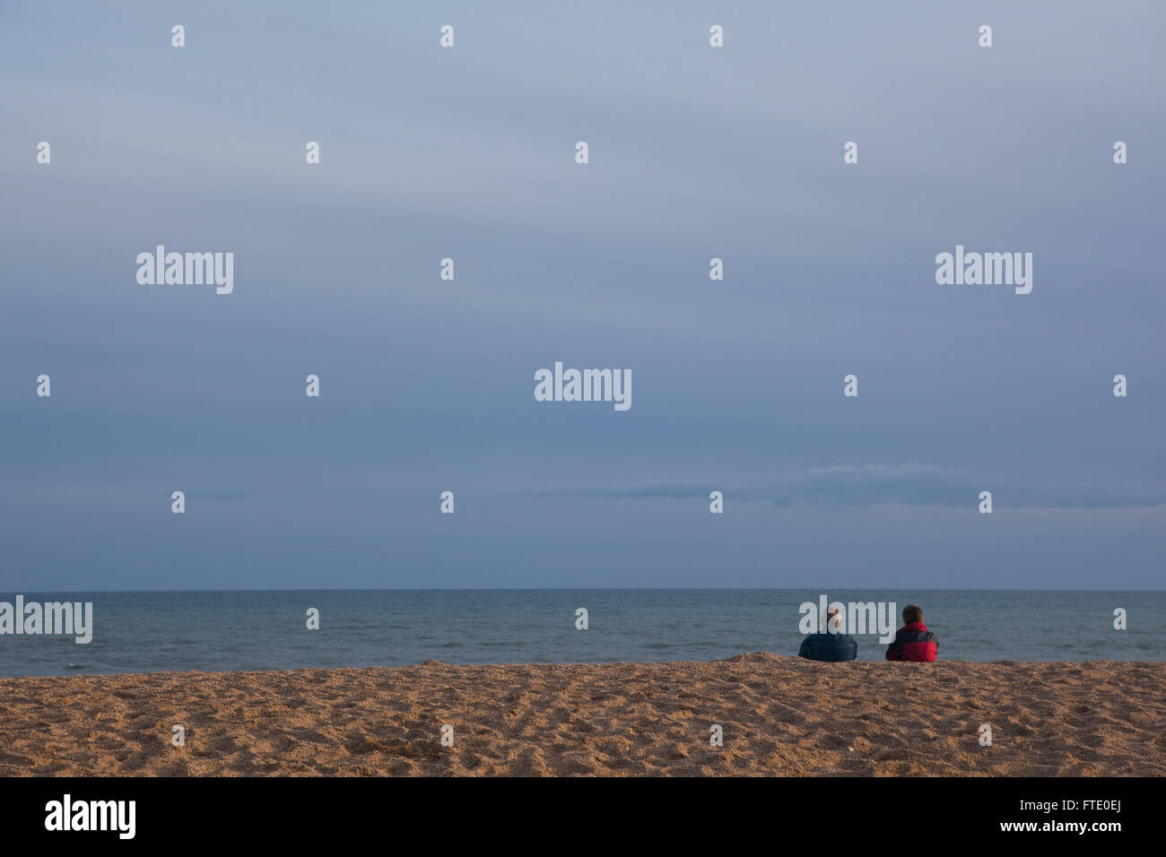 Ein paar wahrscheinlich im Ruhestand oder alten sitzen an einem Strand in der Dämmerung den Sonnenuntergang an der Küste, Ruhe und Kontemplation Leben in dieses friedliche ruhige Szene. Stockfoto