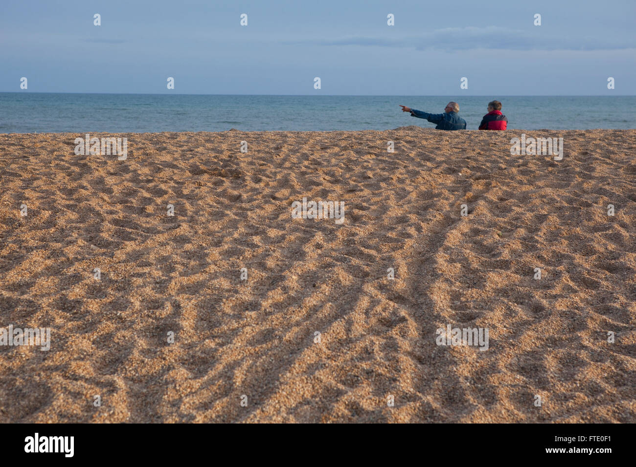 Ein paar wahrscheinlich im Ruhestand oder alten sitzen an einem Strand in der Dämmerung den Sonnenuntergang an der Küste, Ruhe und Kontemplation Leben in dieses friedliche ruhige Szene. Stockfoto