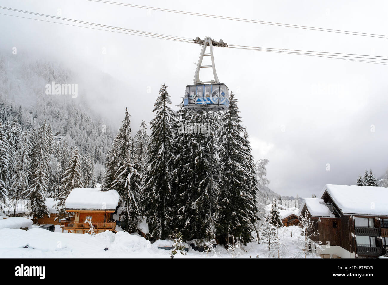 Die Drahtseilbahn Gondel gegen einen verschneiten Tannenwald und die alpinen Häuser Stockfoto
