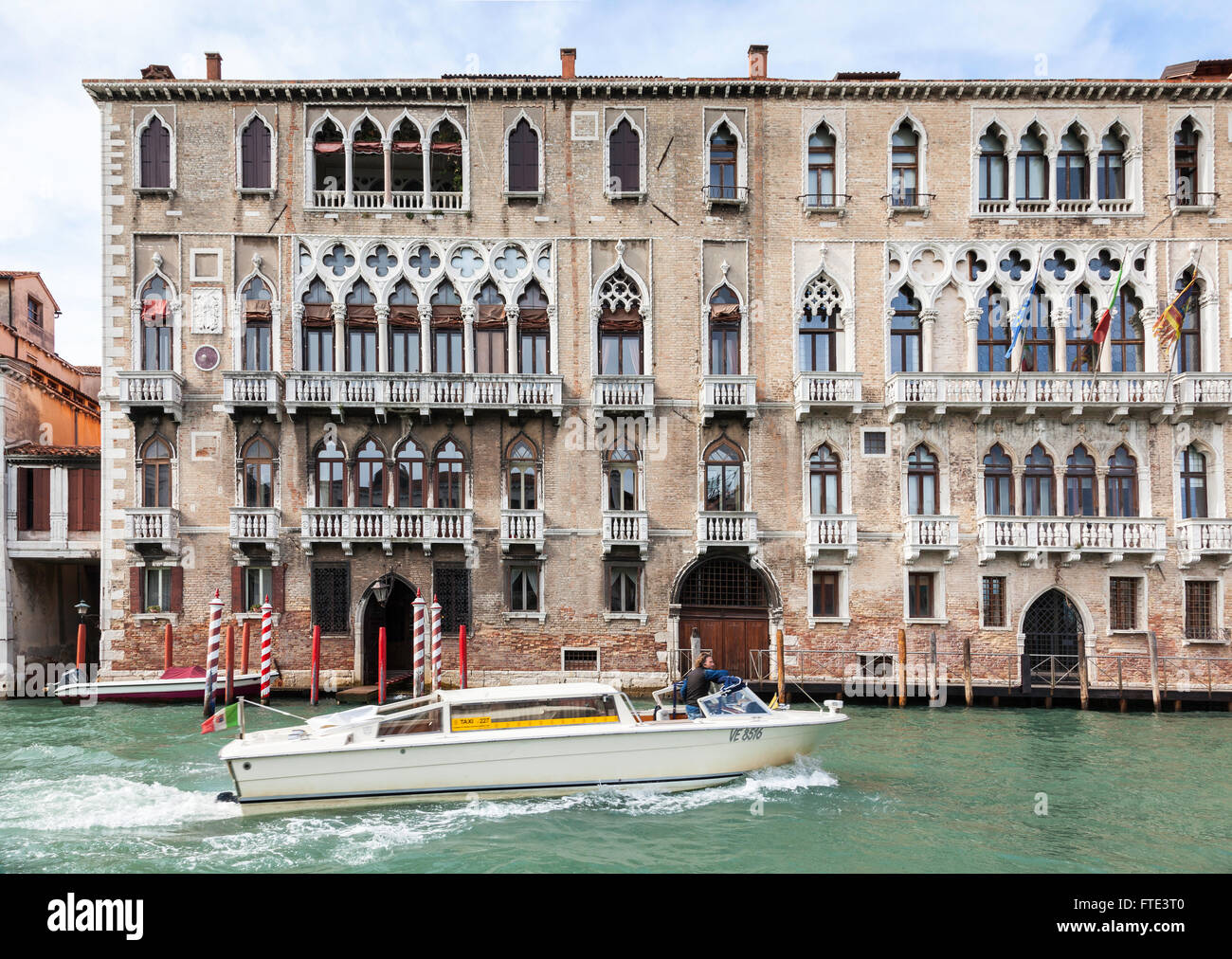 Klassisches Hafengebäude mit verzierten Fenstern und Balkonen mit roten Anlegestellen und einer vorbeifahrenden Bootsanlegestelle auf dem Canal Grande, Venedig, Italien Stockfoto