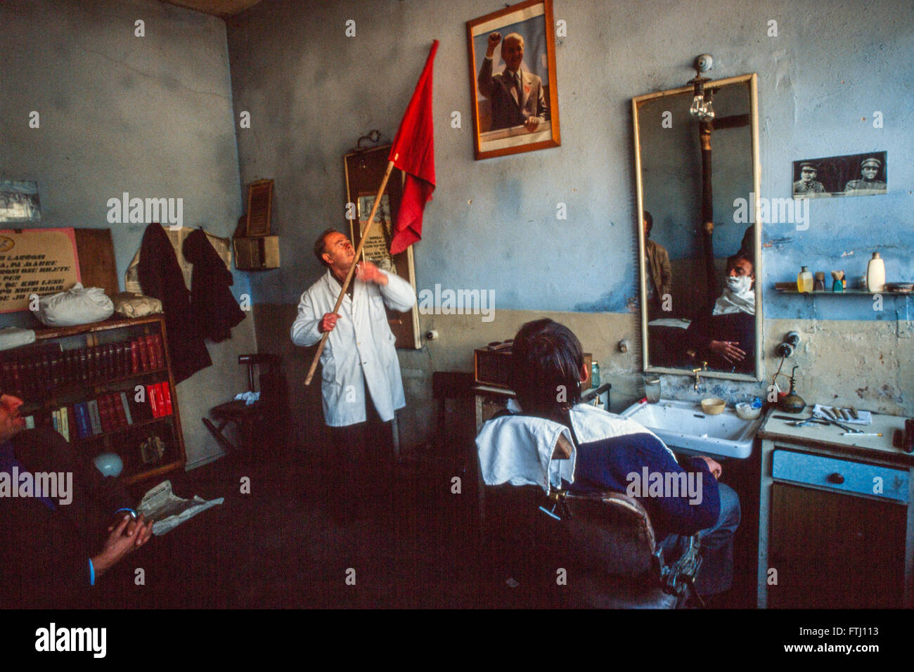 Ein Friseur in Girokaster hält die albanische Flagge während ein Porträt von Enver Hoxha, Gründer des kommunistischen Staates hängt an der Wand. Stockfoto