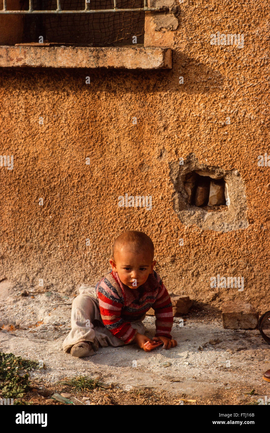 Ein kleiner Junge spielt auf dem Boden vor seinem Haus in Saranda, Albanien. Stockfoto