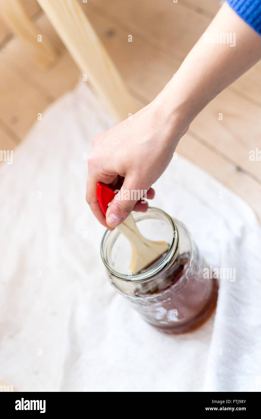 Weibliche Hand taucht einen Pinsel in einem Glas Lack in einem Workshop. Stoff Textur Hintergrund für Designs und nach Hause DIY-Idee Stockfoto