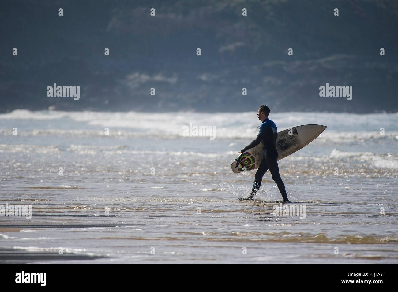 Ein Surfer trägt sein Surfbrett, während er aus dem Meer auf den Fistral Beach in Newquay, Cornwall. Stockfoto
