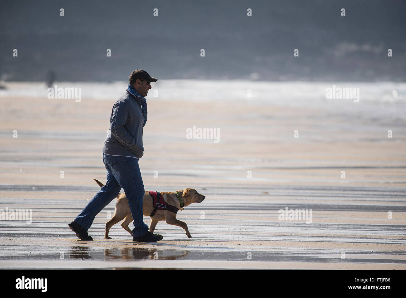 Ein Mann und sein Hund genießen einen flotten Spaziergang am Fistral Beach in Newquay, Cornwall. Stockfoto