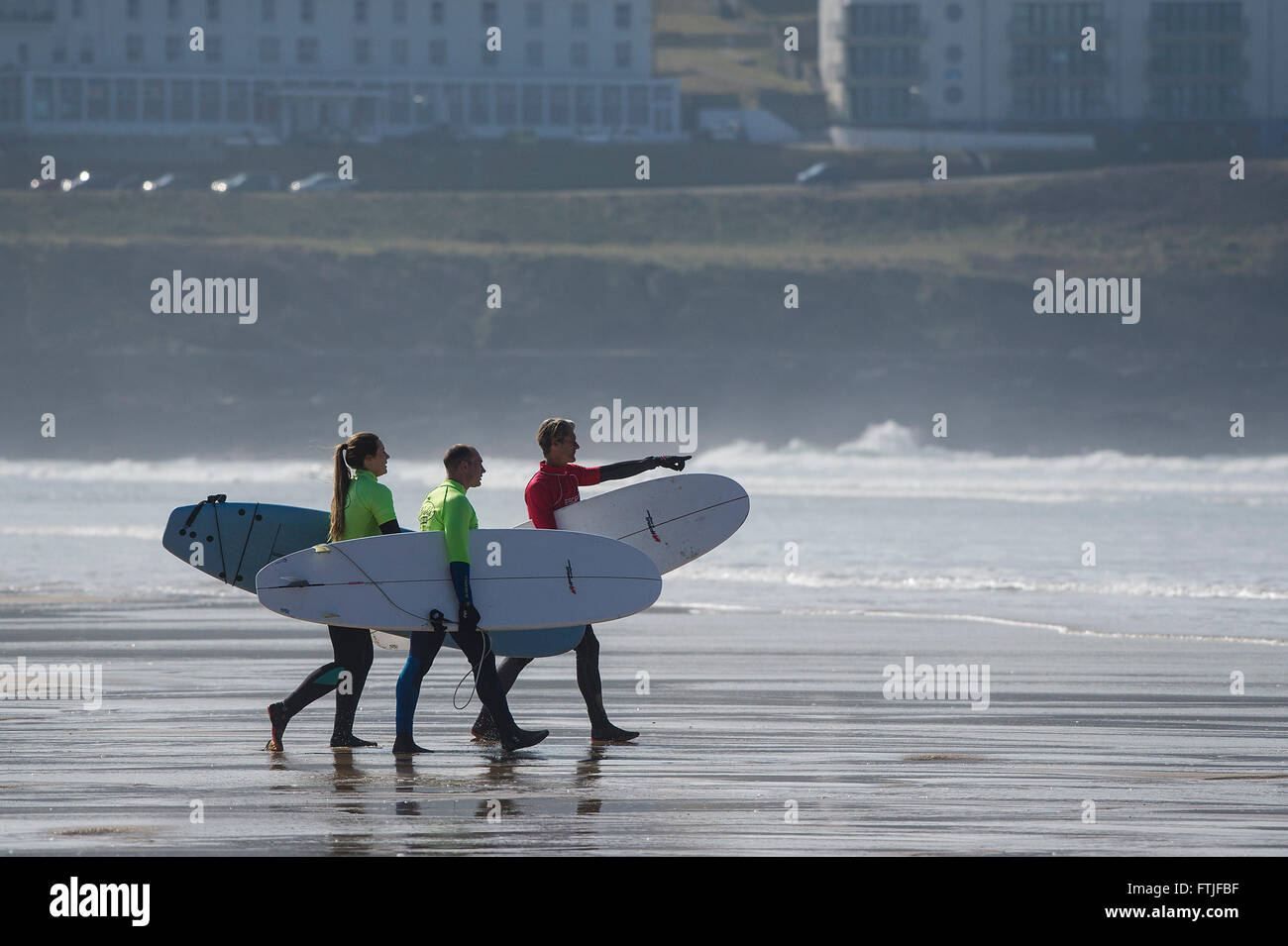 Ein Surflehrer und seine zwei Novizen tragen ihre Surfbretter auf Fistral Beach in Newquay, Cornwall. VEREINIGTES KÖNIGREICH. Stockfoto