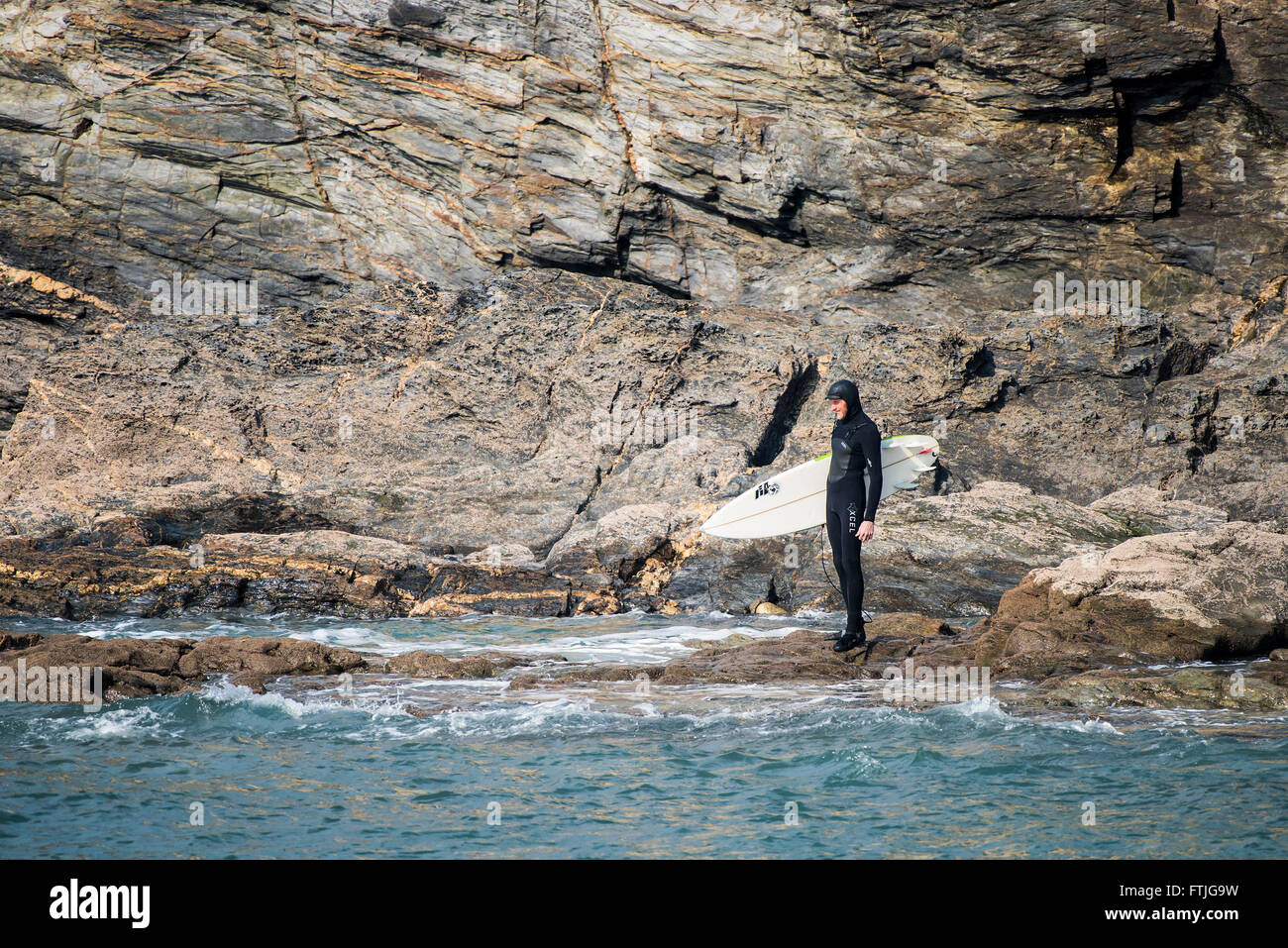 Eine Surfer steht am Fuße der schroffen Klippen und das Meer sieht. Stockfoto