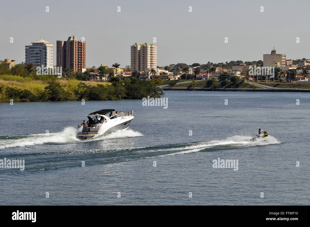 Jetski und Boot fahren in Rio Paranaiba mit Stadt im Hintergrund Stockfoto