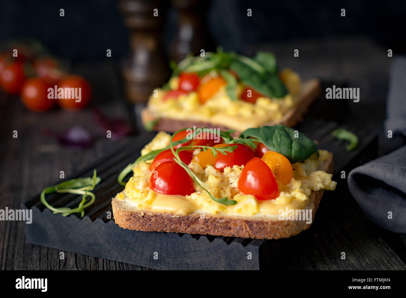 Toast zum Frühstück mit Rührei, Käse, Cherry-Tomaten, Rucola und Feldsalat auf rustikalen hölzernen Hintergrund Stockfoto