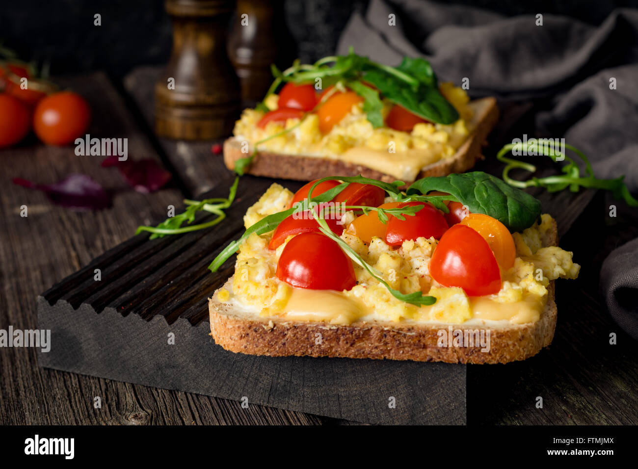Toast zum Frühstück mit Rührei, Käse, Cherry-Tomaten, Rucola und Feldsalat auf rustikalen hölzernen Hintergrund Stockfoto