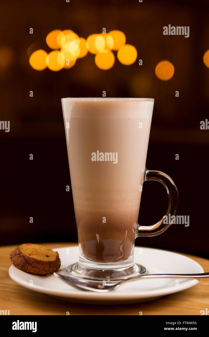 Caffe Macchiato Kaffee trinken in einem langen Glas in einem Café auf eine Untertasse mit einem Keks serviert. Stockfoto