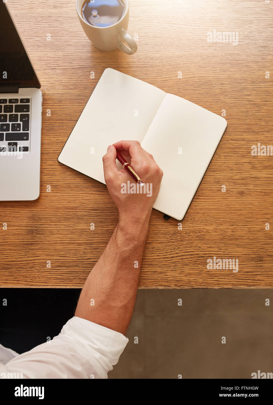 Ansicht von oben Schuss des Mannes einige Notizen in seinem Tagebuch sitzend an seinem Arbeitsplatz. Stockfoto