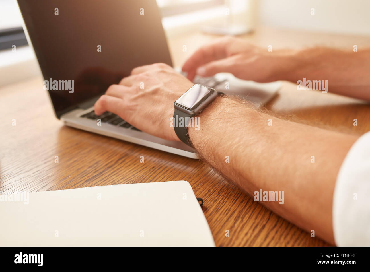 Schließen Sie herauf Bild des Mannes mit einer Smartwatch arbeiten am Laptop sitzt an seinem Schreibtisch. Stockfoto