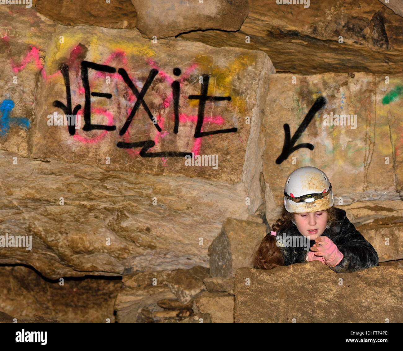 Kind beim Klettern Helm unterirdisch in einem Bergwerk, von 'Exit' Zeichen. Eine Spray lackiert Wegweiser in einem stillgelegten Kalkstein mine Stockfoto