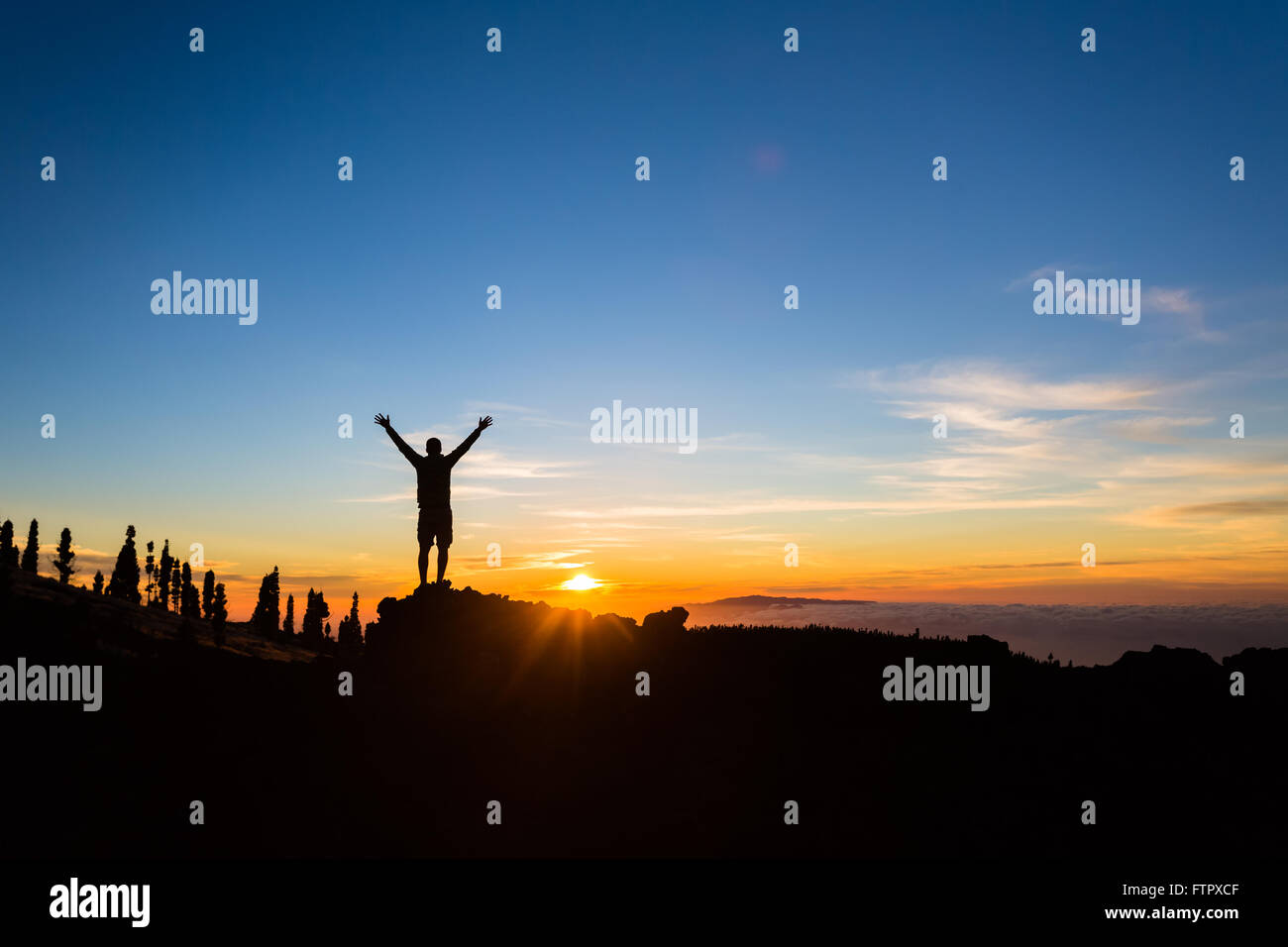Mann-Wanderer-Silhouette mit ausgestreckten in Bergen. Männliche Läufer oder Kletterer, die Aussicht auf den Sonnenuntergang betrachten. Business-Konzept Stockfoto