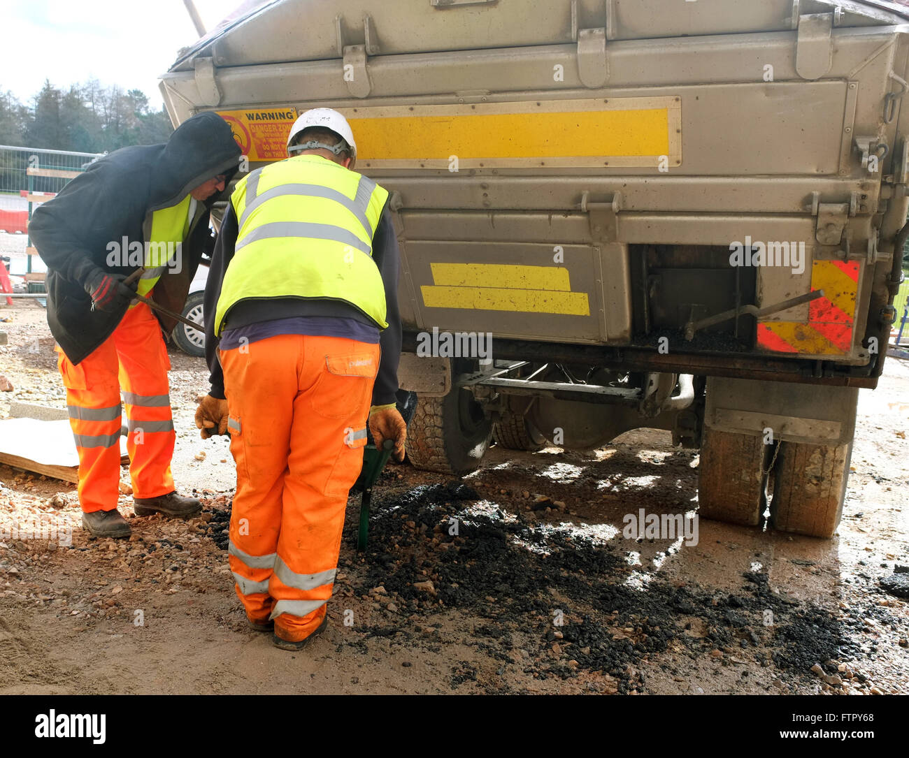 Männer, die Asphalt Asphalt aus dem hinteren Teil eines Kipp LKW während der Arbeit am Gehweg Pflaster. März 2016 Stockfoto