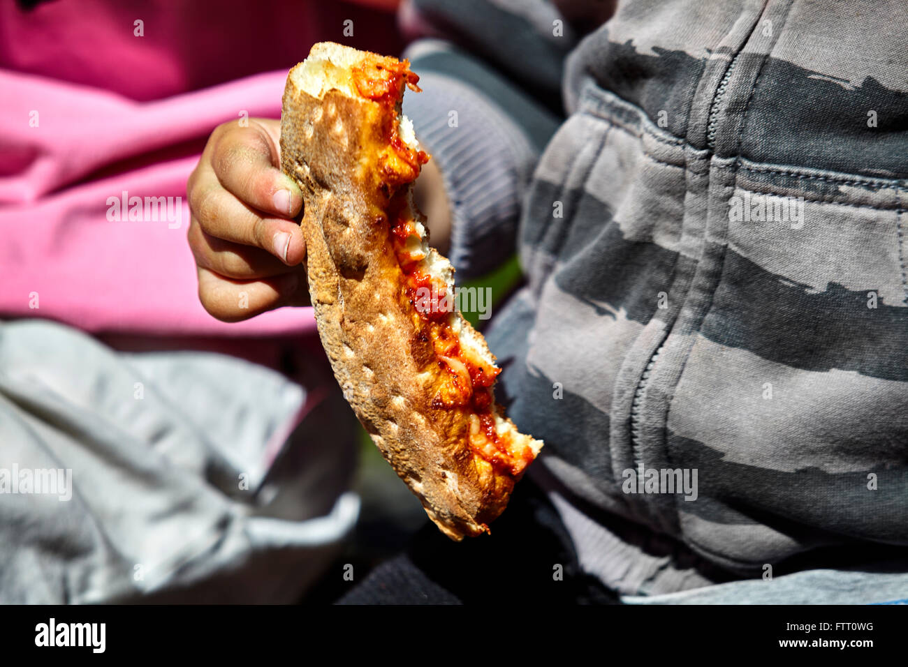 Junge Kind hält eine teilweise gegessen Pizza-Kruste mit einer grauen Jacke an und geringe Schärfentiefe Stockfoto