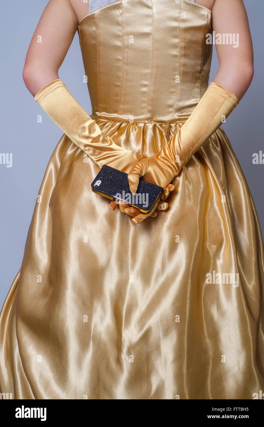 junge Frau in gold Kleid halten Iphone hinter Rücken Stockfoto