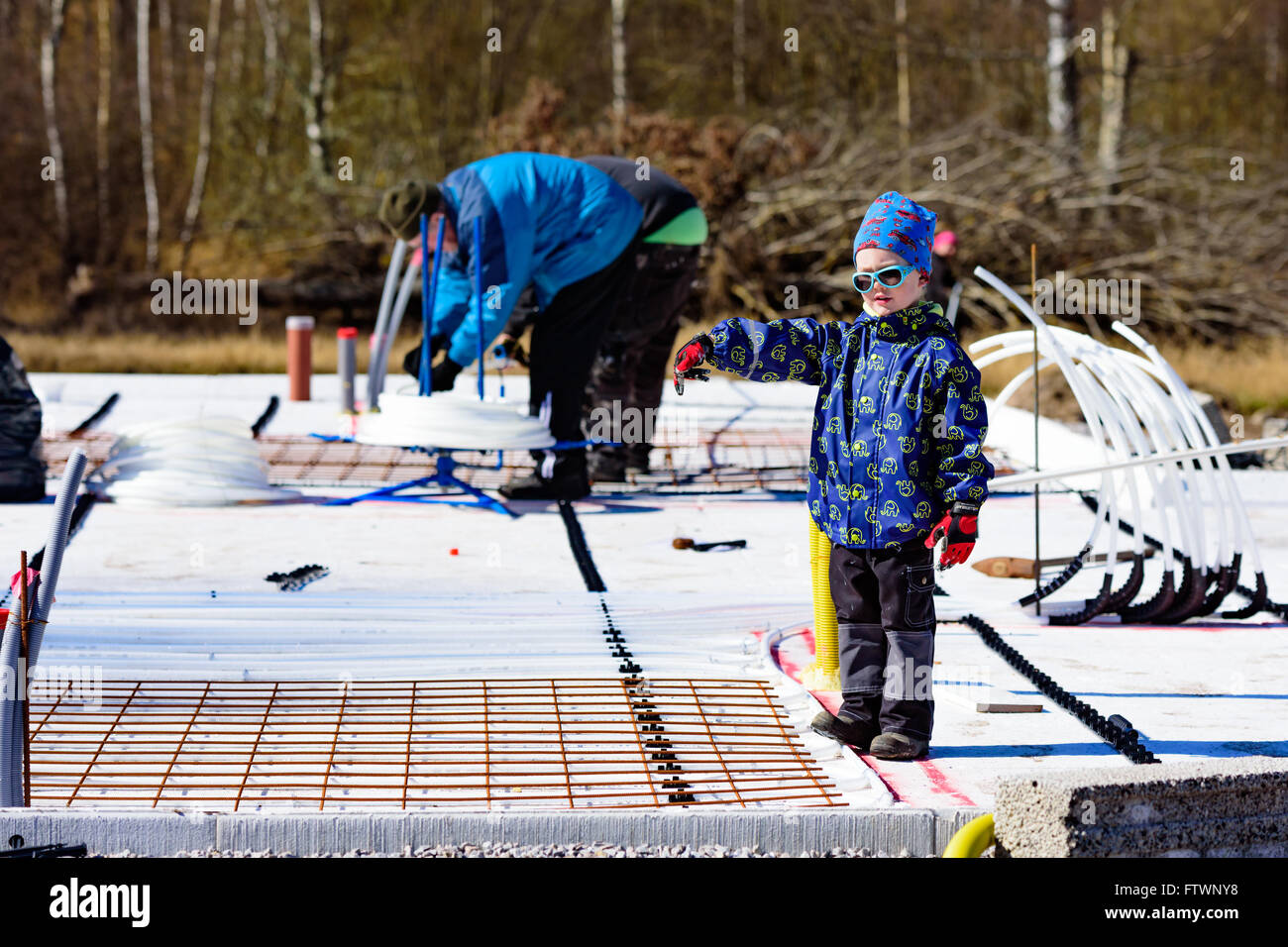 Ronneby, Schweden - 26. März 2016: Junge Regie und deutete auf eine Baustelle. Erwachsene im Hintergrund arbeiten. Junge wea Stockfoto